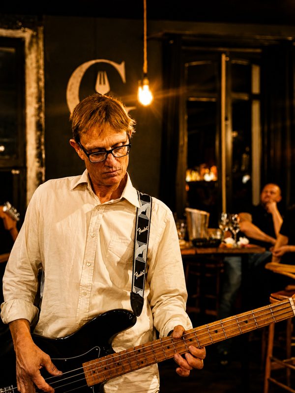 Alambic Brothers — Bassiste en chemise blanche jouant dans une salle de concert