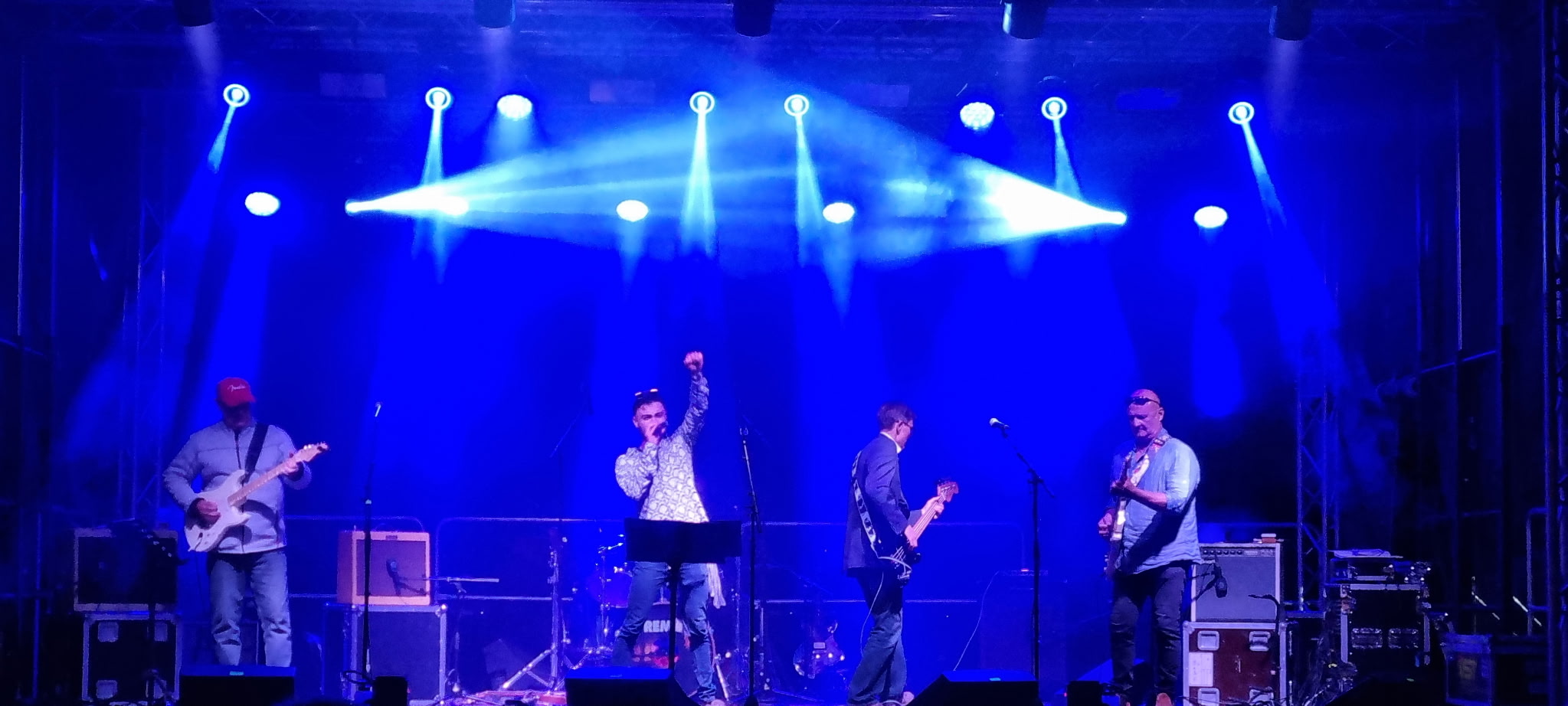 Le groupe sur scène sous des projecteurs bleus, Émile au micro, le poing levé.